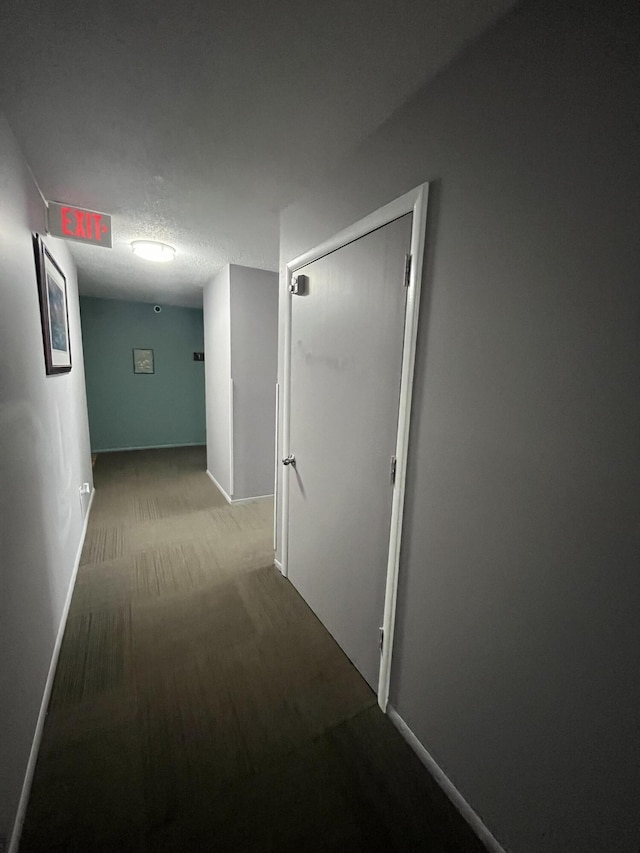 corridor with light colored carpet, a textured ceiling, and baseboards