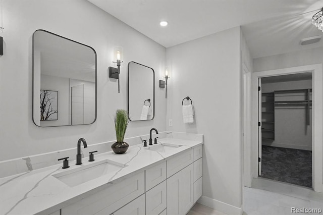 full bath with double vanity, a spacious closet, a sink, and baseboards