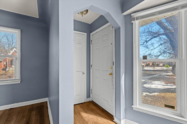 foyer entrance with light wood-type flooring, arched walkways, and baseboards