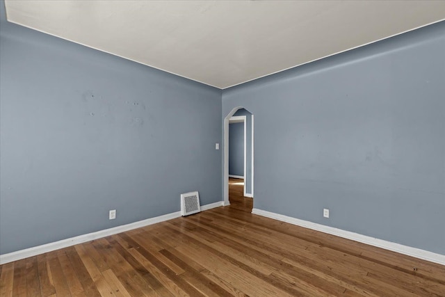 unfurnished room featuring arched walkways, visible vents, baseboards, and hardwood / wood-style flooring