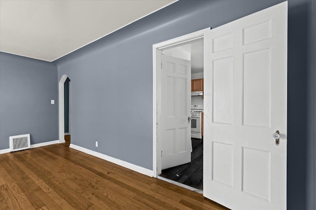 unfurnished room featuring arched walkways, hardwood / wood-style floors, visible vents, and baseboards