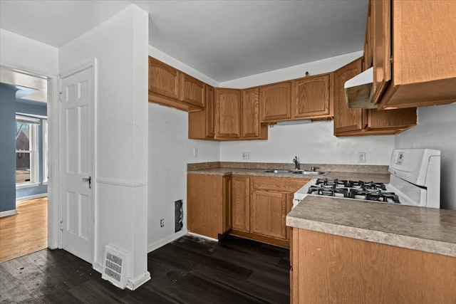 kitchen with white range with gas cooktop, brown cabinetry, dark wood-style floors, light countertops, and a sink