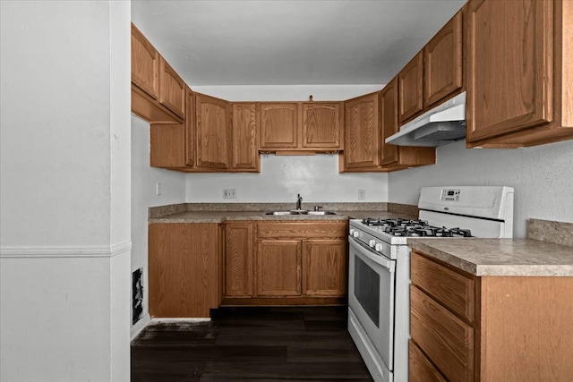 kitchen featuring brown cabinetry, white gas stove, under cabinet range hood, and a sink