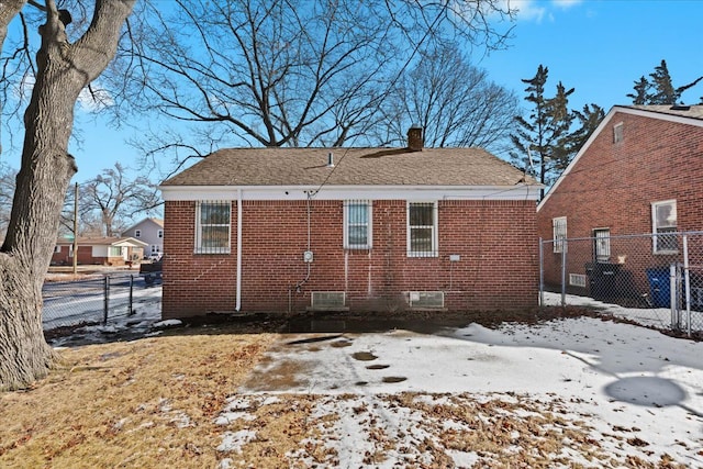 snow covered back of property featuring brick siding, fence, and a chimney