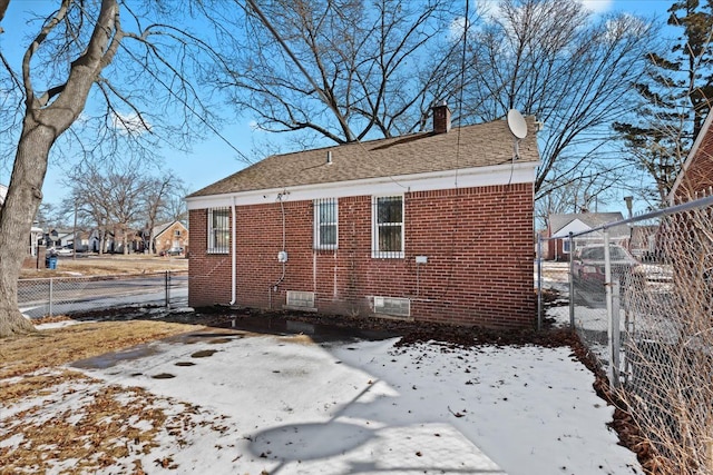 snow covered property featuring crawl space, brick siding, a chimney, and fence