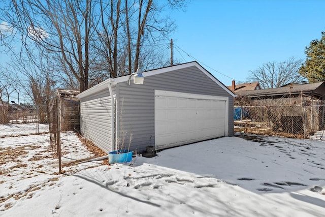 snow covered garage featuring a garage and fence