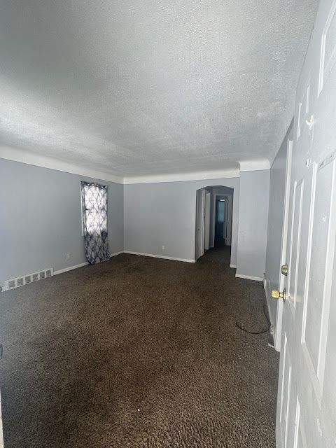 empty room featuring baseboards, visible vents, dark carpet, and a textured ceiling