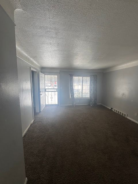 carpeted empty room with visible vents, a textured ceiling, and baseboards