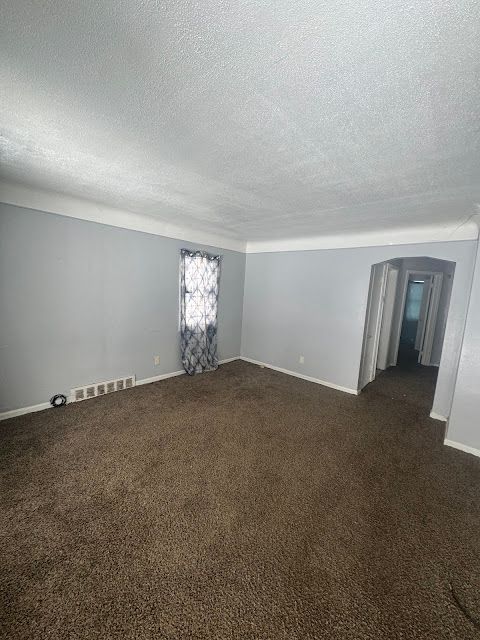 spare room featuring dark colored carpet, visible vents, a textured ceiling, and baseboards