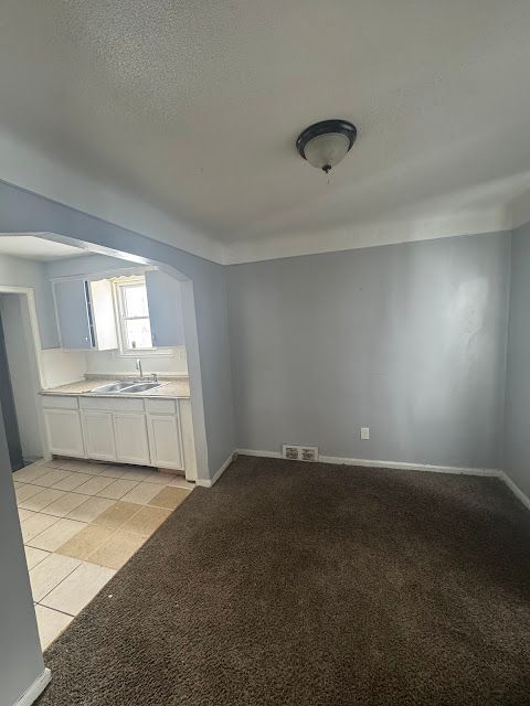 unfurnished dining area featuring light carpet, light tile patterned floors, visible vents, a textured ceiling, and a sink