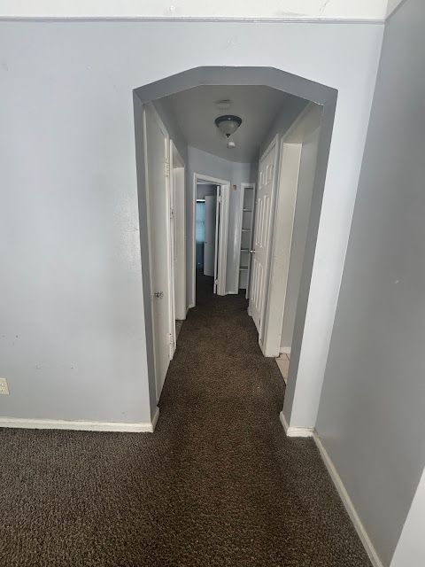 hall with arched walkways, dark carpet, and baseboards