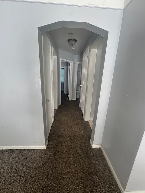 hall featuring baseboards, arched walkways, and dark colored carpet