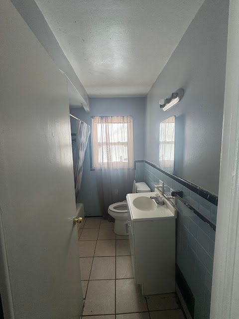 full bathroom featuring tile patterned flooring, a wainscoted wall, vanity, and tile walls