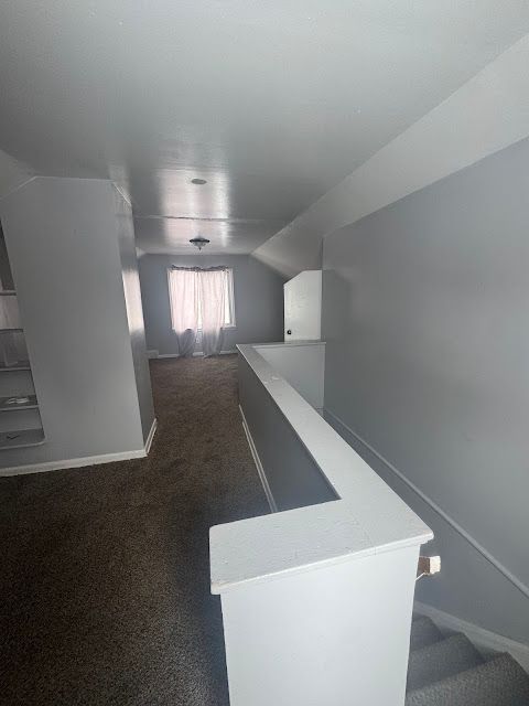 hallway with lofted ceiling, dark carpet, and baseboards