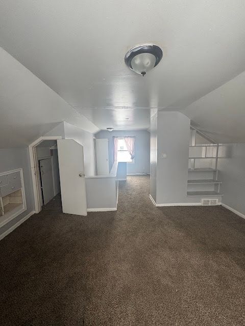 bonus room featuring dark carpet, vaulted ceiling, and baseboards