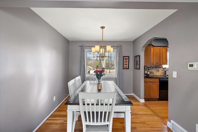 dining area with light wood finished floors, baseboards, arched walkways, and an inviting chandelier