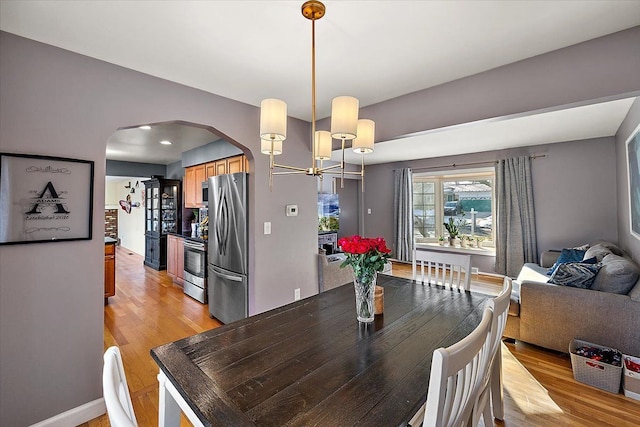 dining area featuring arched walkways, baseboards, and light wood finished floors