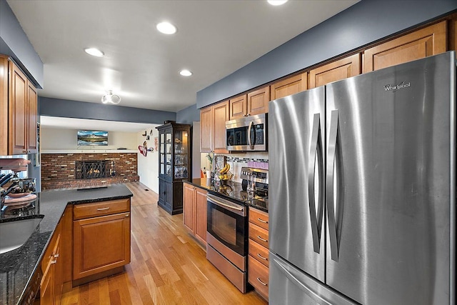 kitchen featuring stainless steel appliances, a brick fireplace, brown cabinetry, and light wood-style floors