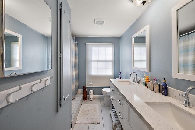 bathroom with visible vents, double vanity, a sink, and toilet