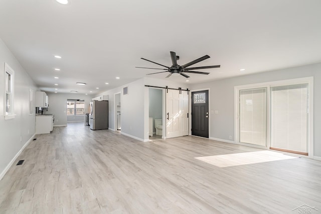 unfurnished living room featuring light wood-type flooring, a barn door, visible vents, and recessed lighting