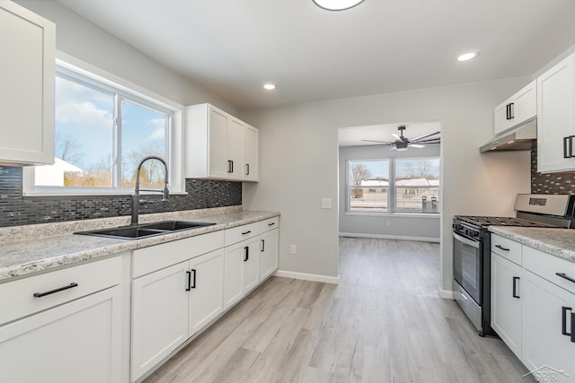 kitchen featuring under cabinet range hood, a sink, white cabinets, light stone countertops, and stainless steel gas stove