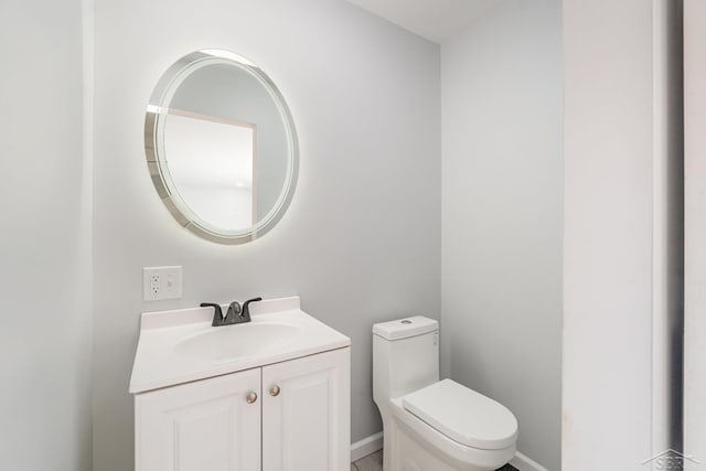 half bath featuring baseboards, vanity, and toilet