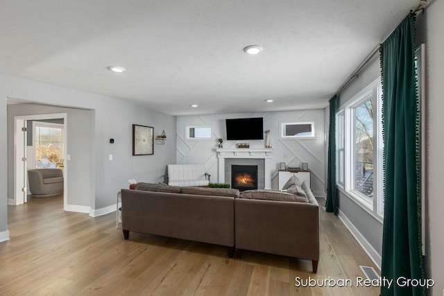 living room with recessed lighting, light wood-style floors, a glass covered fireplace, a textured ceiling, and baseboards