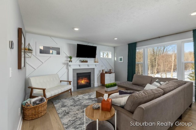 living area featuring recessed lighting, light wood-style flooring, a textured ceiling, and a fireplace with flush hearth