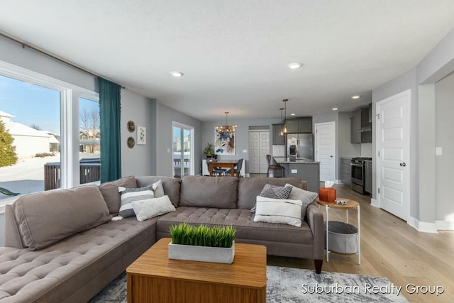 living area featuring light wood-style flooring, baseboards, a notable chandelier, and recessed lighting