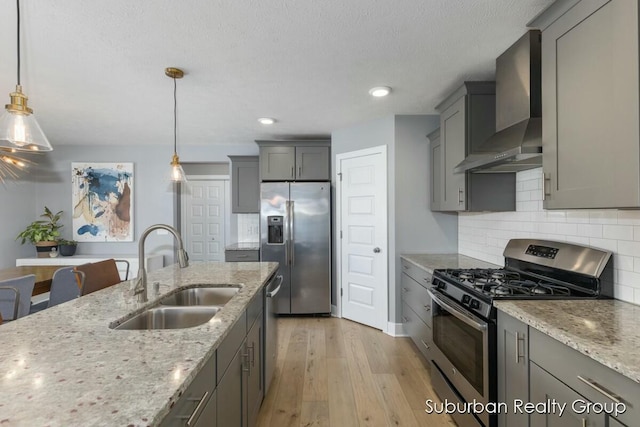 kitchen with pendant lighting, appliances with stainless steel finishes, a sink, wall chimney range hood, and light stone countertops