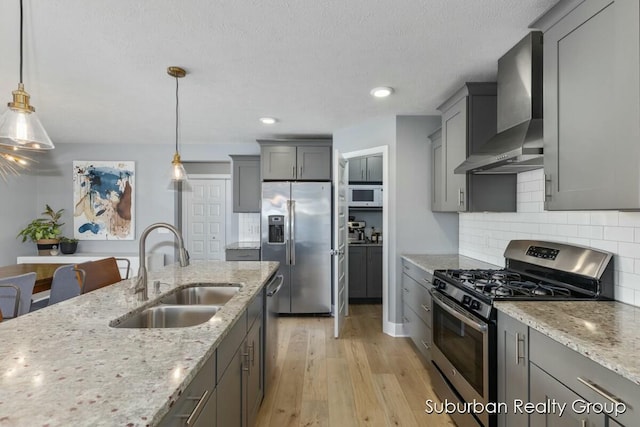 kitchen featuring wall chimney exhaust hood, light stone counters, stainless steel appliances, pendant lighting, and a sink