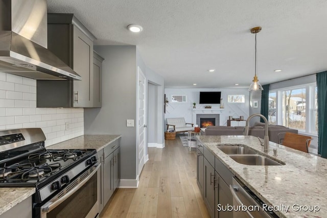 kitchen featuring stainless steel gas range oven, light stone counters, open floor plan, wall chimney range hood, and a sink