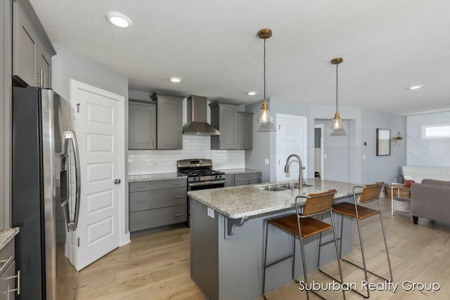 kitchen featuring hanging light fixtures, gray cabinets, stainless steel appliances, wall chimney range hood, and a sink