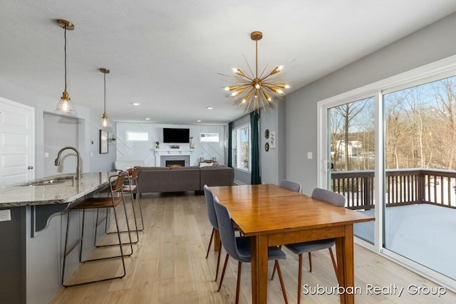 dining space with a warm lit fireplace, light wood finished floors, a notable chandelier, and recessed lighting