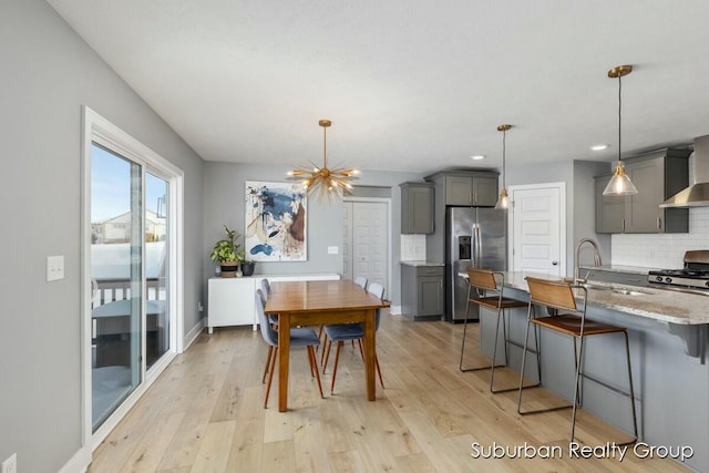 kitchen featuring light wood finished floors, hanging light fixtures, stainless steel appliances, gray cabinetry, and backsplash