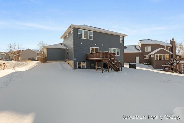 snow covered back of property with a deck, stairway, and a detached garage