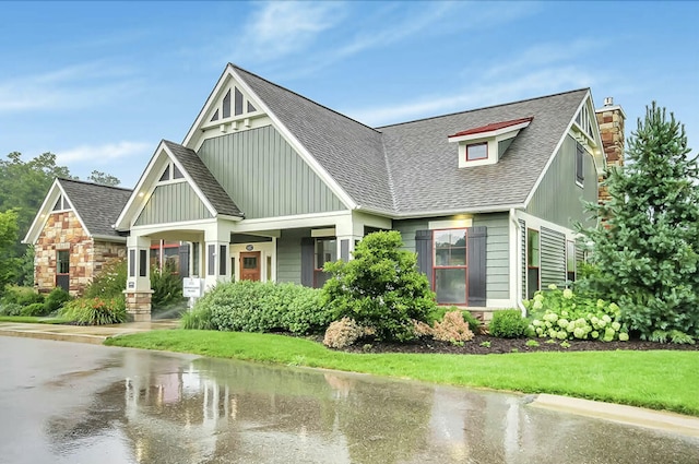 craftsman inspired home with stone siding, a shingled roof, a chimney, and a front yard