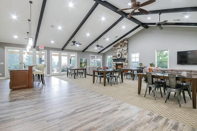 dining space with light wood-style floors, a fireplace, high vaulted ceiling, and beamed ceiling