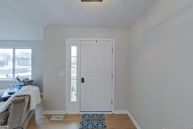 foyer entrance with visible vents, light wood-style flooring, and baseboards