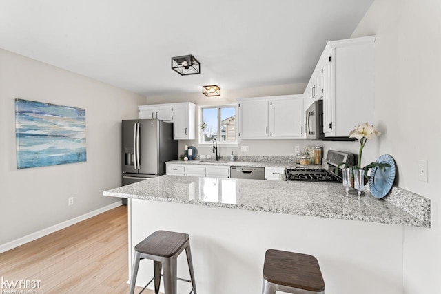 kitchen with a breakfast bar area, stainless steel appliances, a peninsula, a sink, and light wood finished floors