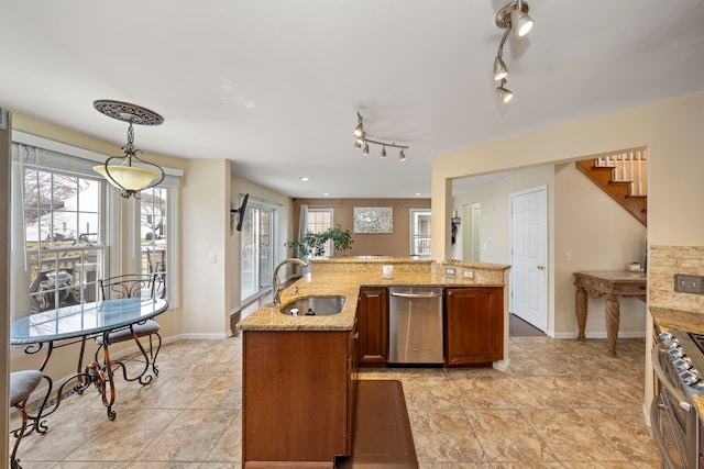 kitchen with light stone counters, hanging light fixtures, appliances with stainless steel finishes, brown cabinetry, and a sink