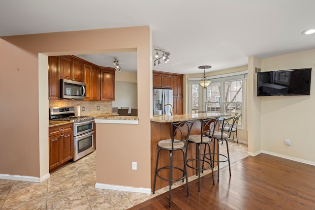 kitchen featuring tasteful backsplash, baseboards, appliances with stainless steel finishes, a breakfast bar, and light stone counters