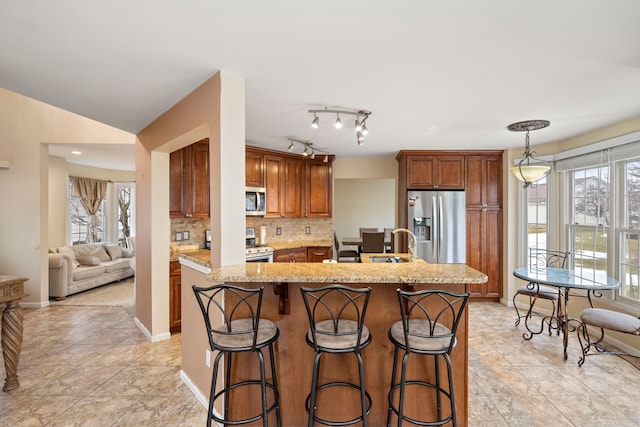 kitchen with a kitchen breakfast bar, appliances with stainless steel finishes, backsplash, light stone countertops, and a center island with sink