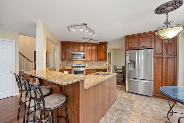 kitchen featuring light stone counters, backsplash, appliances with stainless steel finishes, a sink, and a kitchen bar