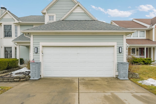 traditional home with a garage, concrete driveway, and roof with shingles