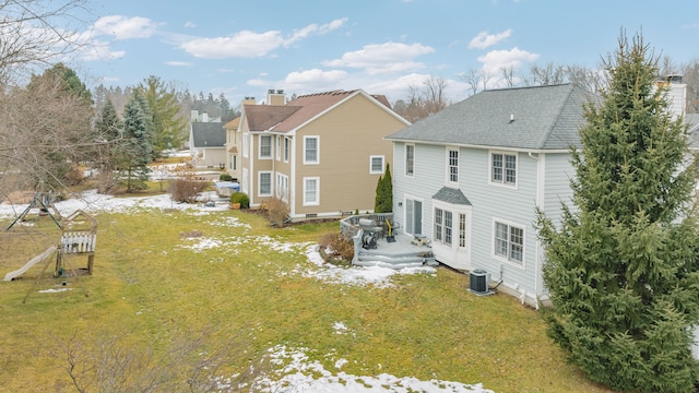 back of house featuring central AC, a shingled roof, a lawn, and a playground