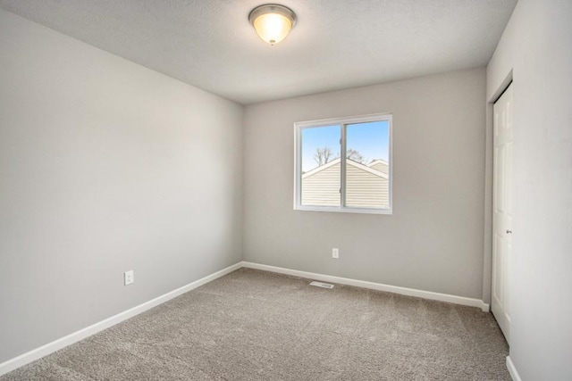 carpeted spare room featuring visible vents, a textured ceiling, and baseboards