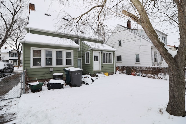 snow covered rear of property featuring entry steps and fence