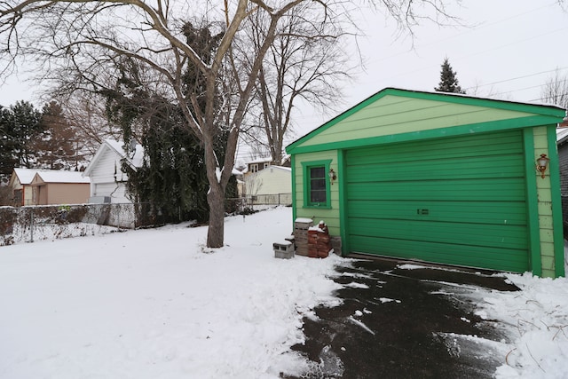 snow covered garage featuring a garage and fence