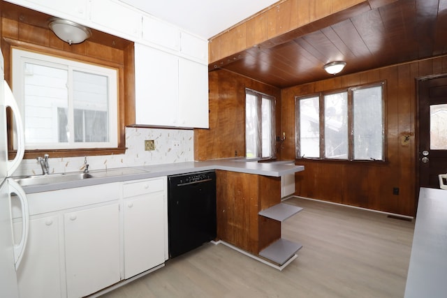 kitchen with wood walls, a sink, white cabinets, black dishwasher, and light countertops